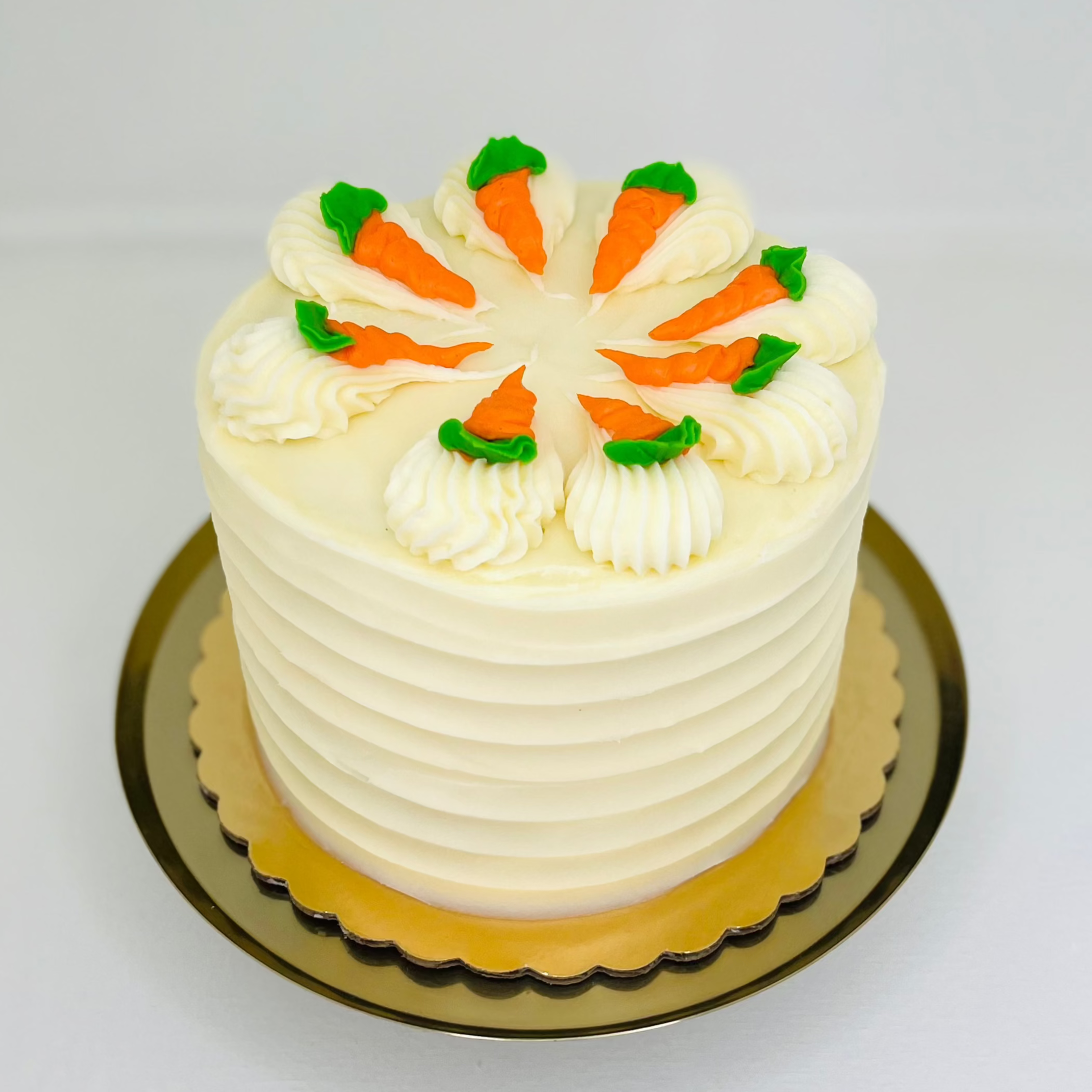 A 6-inch round carrot cake with cream cheese icing, decorated with orange and green icing to resemble carrots, placed on a gold platter.