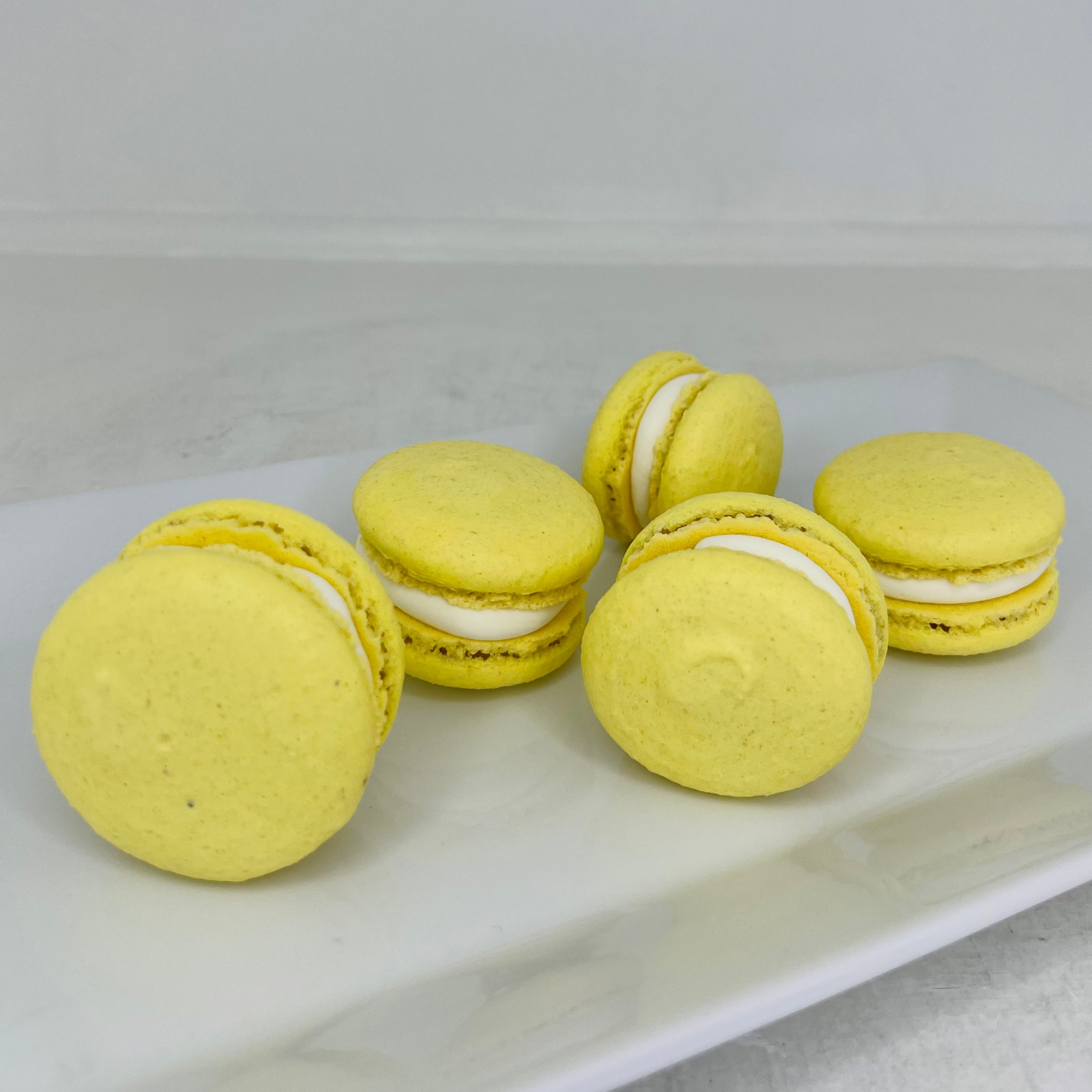 Yellow macarons with white filling on a white plate against a light gray background