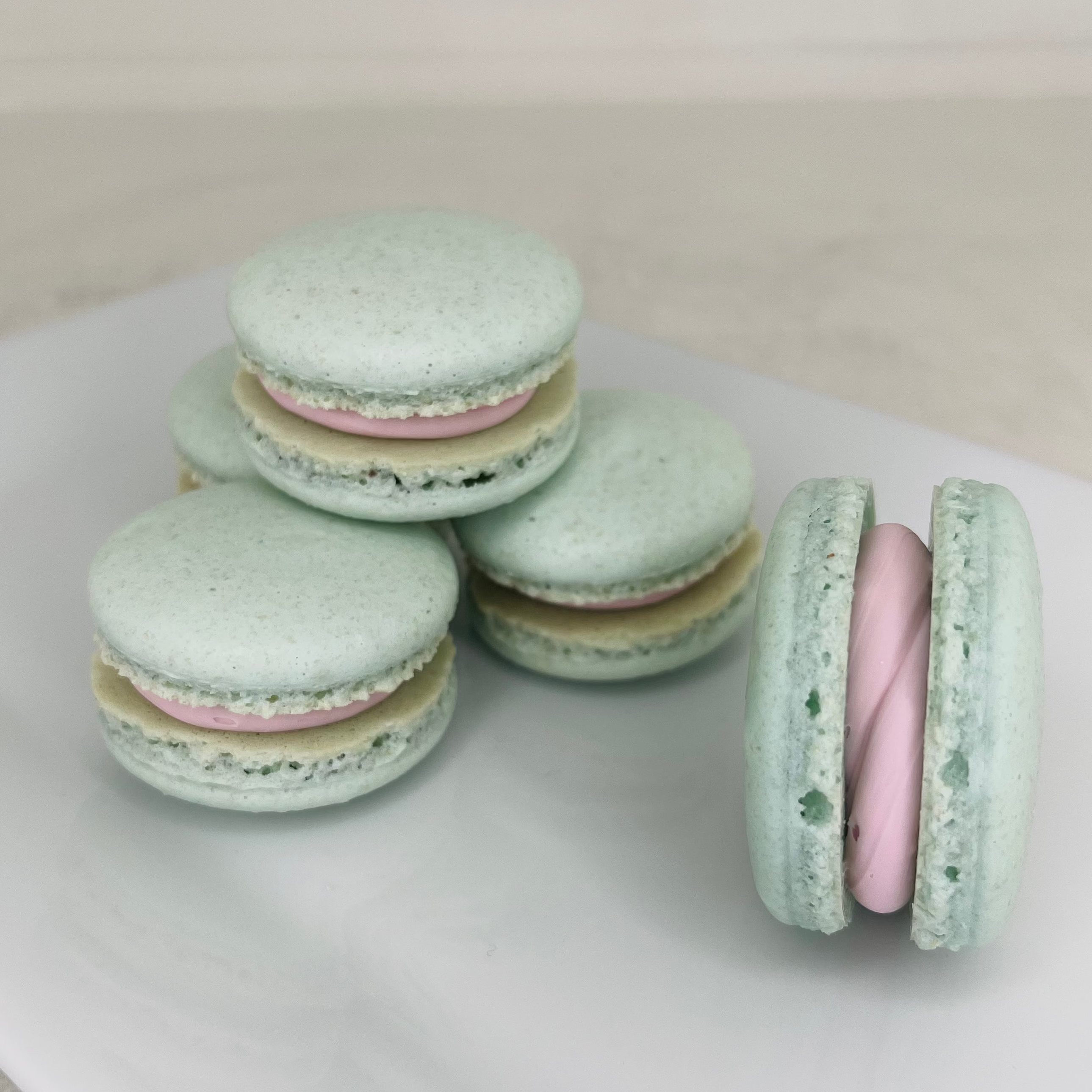 Pastel green macarons with pink filling on a white surface