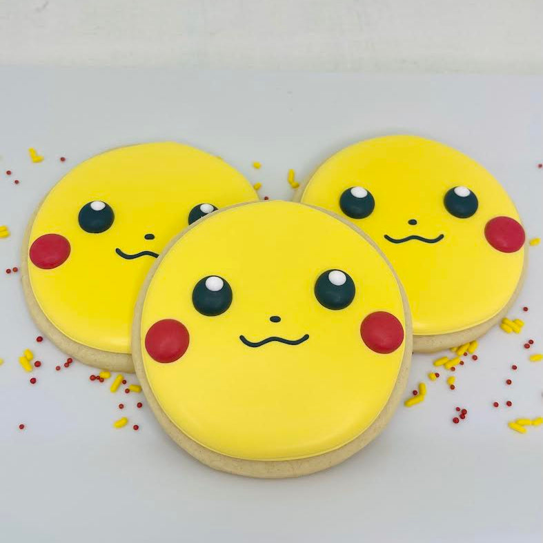 Three cookies shaped like Pikachu with yellow faces, black eyes, and red cheeks on a white background.