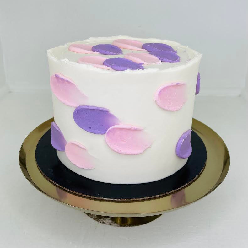 White cake with pink and purple brushed strokes on a gold cake stand against a white background