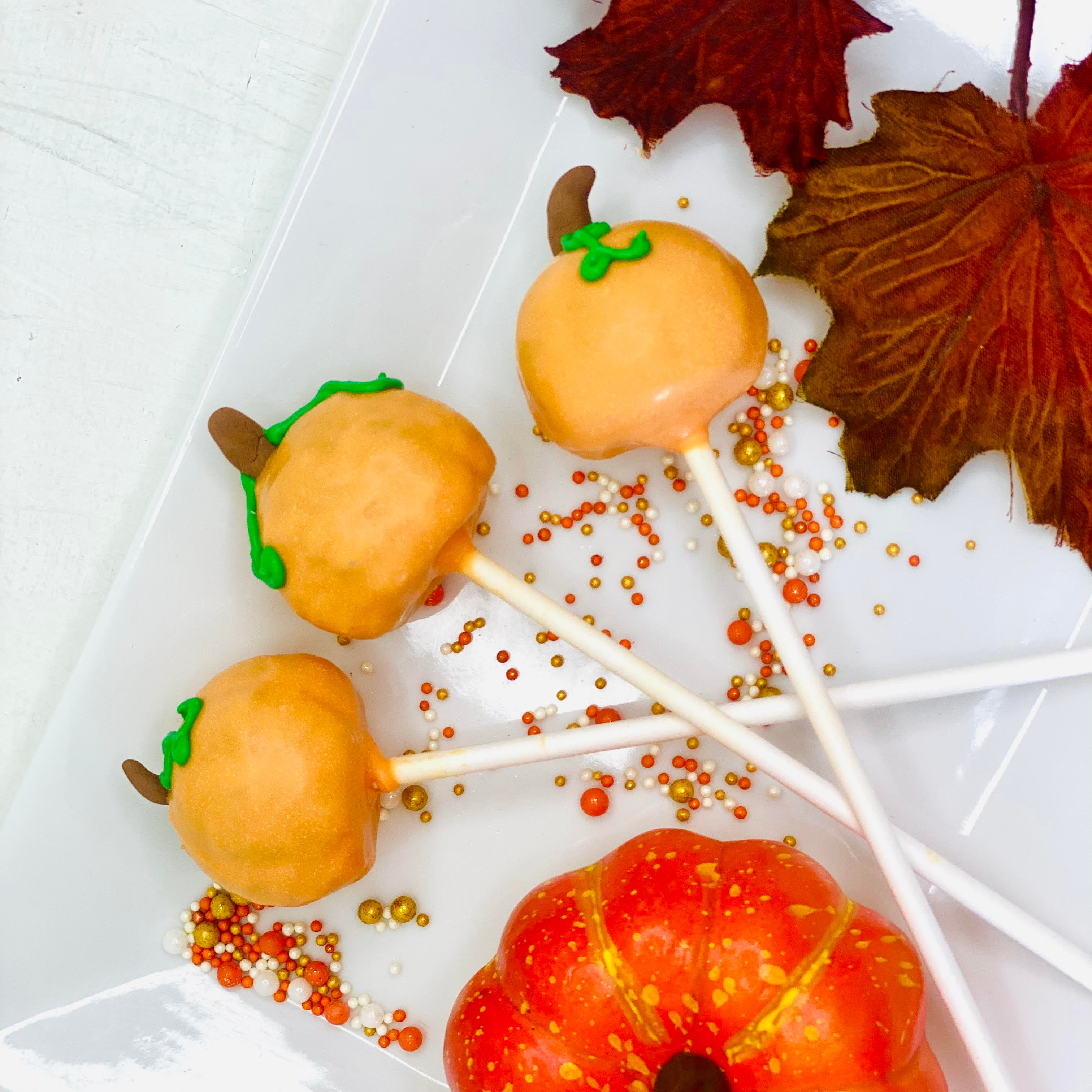 Pumpkin-shaped cake pops on a white plate with decorative leaves.