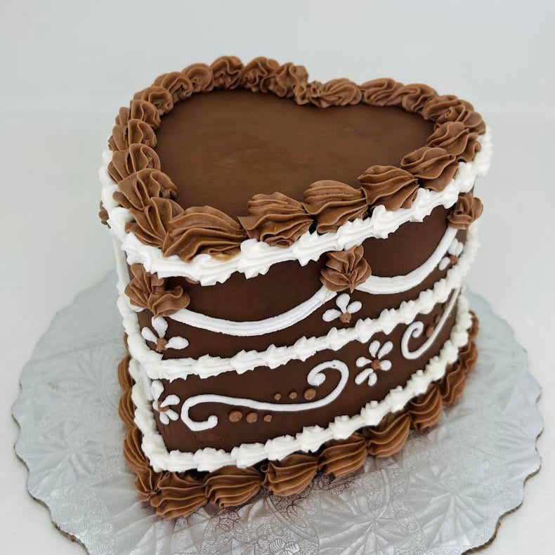 Three-layered chocolate buttercream red velvet cake with white piping on a decorative silver cake stand.