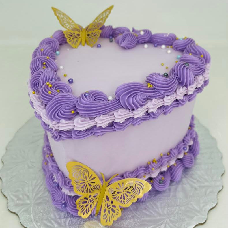 Purple heart cake with yellow butterfly decorations on a white plate.