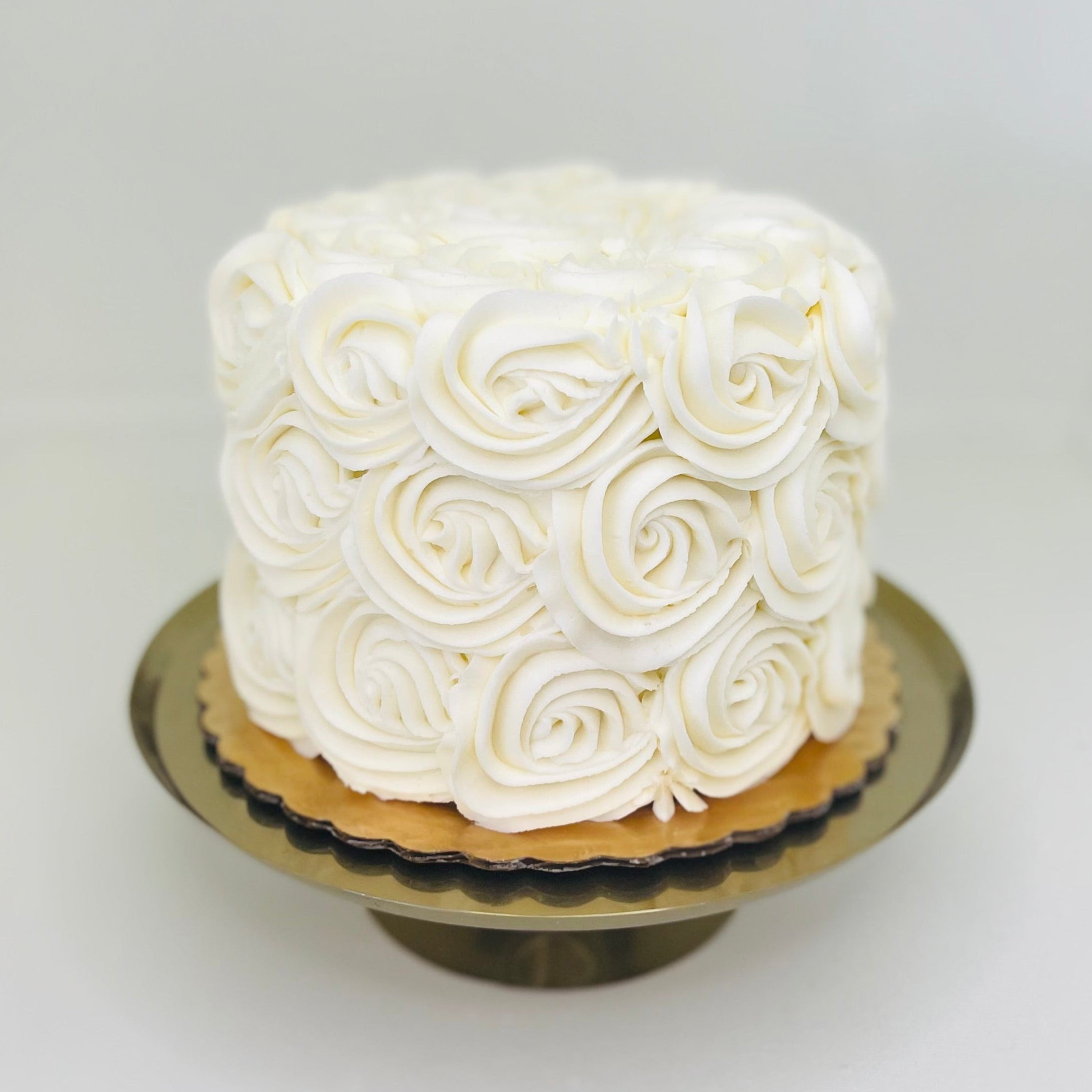 A 6 inch round buttercream rosette cake with white chocolate frosting on a platter.