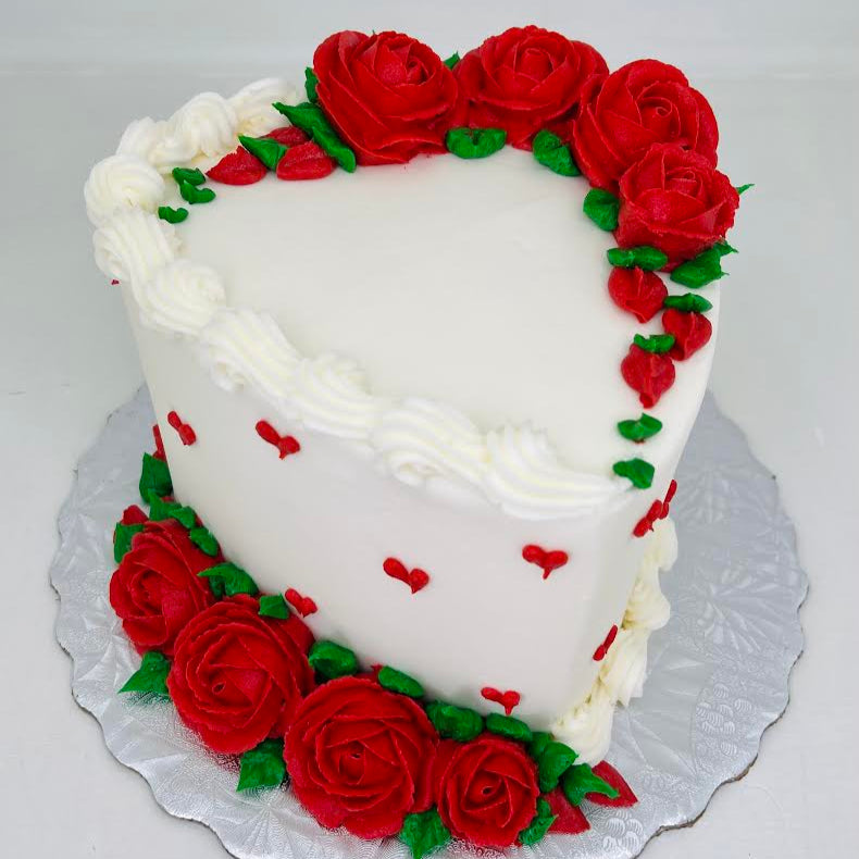 Heart-shaped cake decorated with red roses and green leaves on a white background