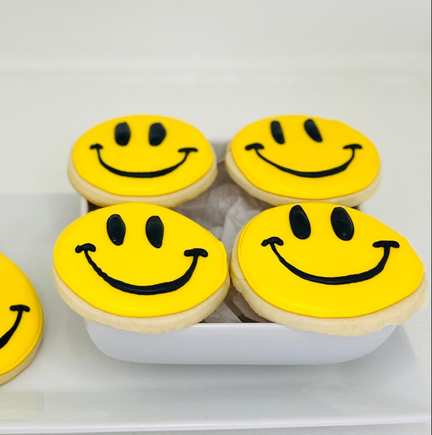 Six yellow smiley face cookies on a white plate with a white background
