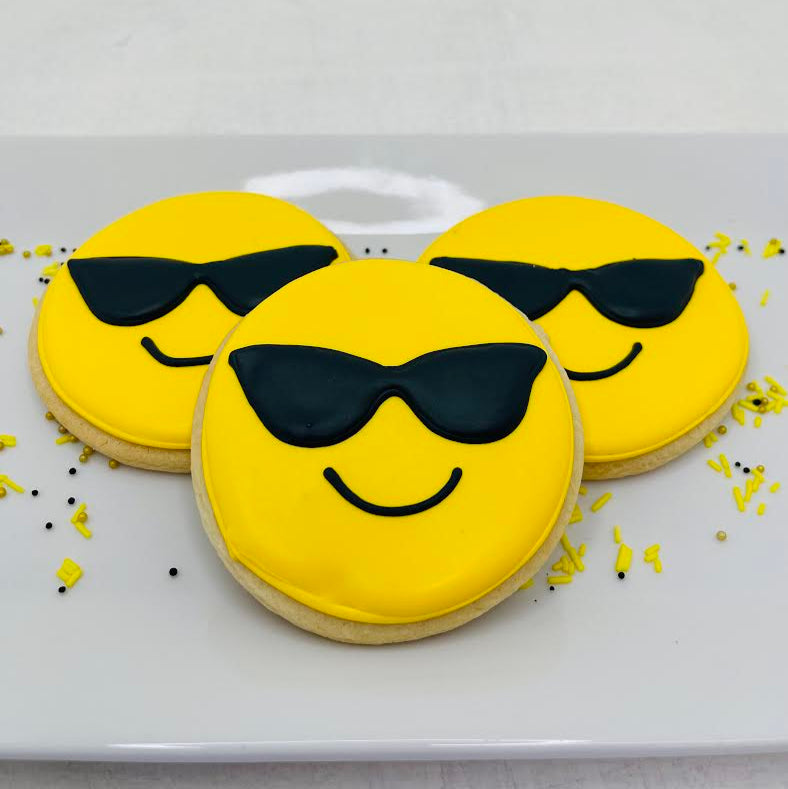 Three cookies with yellow faces and black sunglasses on a white plate.